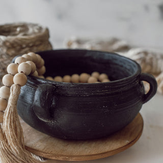 Black ceramic bowl with handles on a wooden stand, surrounded by decorative elements.