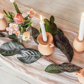 Decorative setting with candles in wooden holders, flowers, and leaves on a textured surface.