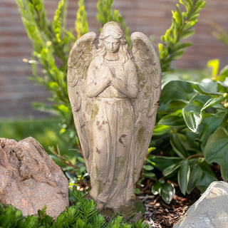 Distressed resin angel garden statue with praying hands, outdoor spiritual décor among rocks and greenery