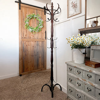 Vintage wood and iron coat rack displayed in a cozy farmhouse entryway with a sliding barn door and floral decor