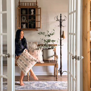 Farmhouse entryway featuring decorative coat rack beside bench and cabinet, with a woman holding a patterned pillow.