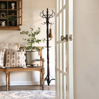 Tall wooden coat rack with iron hooks styled beside rustic bench and wall cabinet in bright farmhouse foyer.