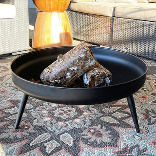 Modern black iron fire pit bowl with wood logs displayed on an outdoor patterned rug, perfect for patio decor