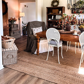 Dining room with wooden table, chairs, and decorative elements on a jute rug.