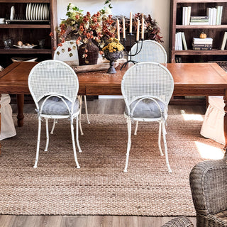 Dining room with jute rug, wooden table, white chairs, and decorative elements.