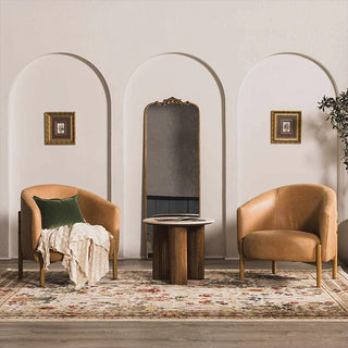 Two brown armchairs with a small table and mirror in a room with arches and framed pictures.