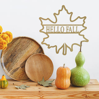 Gold metal maple leaf sign with “Hello Fall” design, displayed with pumpkins and rustic wood trays