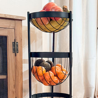 Close-up view of the top two baskets of a three-tier black metal fruit stand filled with apples, bananas, oranges, and avocados.