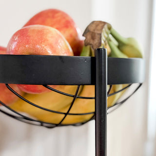 Close-up detail of the top basket of a black metal fruit stand with apples and bananas.