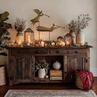 Farmhouse-style Christmas mantel decor featuring metal angel sculptures, lanterns, candles, and greenery on a rustic wood sideboard
