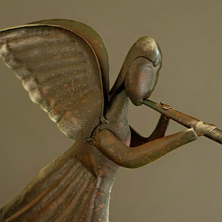 Close-up of distressed metal angel figurine with wings and trumpet, handcrafted rustic holiday decor