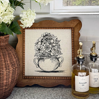 Framed floral artwork on a surface with olive oil bottles and flowers.