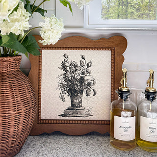 Decorative framed print with floral design next to bottles of avocado and olive oil on a countertop.