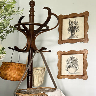 Wooden coat rack with baskets and framed botanical prints on a wall.
