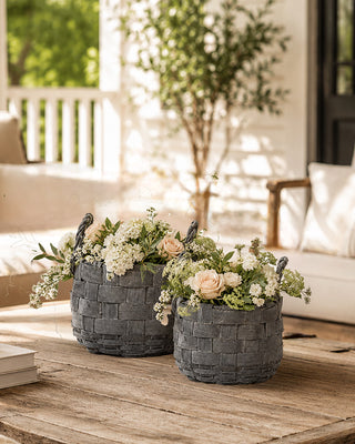 Two woven planters with flowers on a wooden surface outdoors.