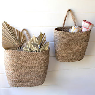  Set of two seagrass hanging baskets in different sizes filled with books and towels against white shiplap wall