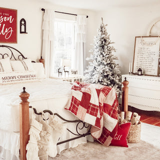  Red and white plaid patchwork Christmas quilt draped over vintage metal bed frame in farmhouse bedroom with flocked Christmas tree