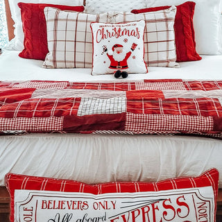 Red plaid Christmas bedding styled on white bed with festive holiday pillows and Santa Claus throw pillow
