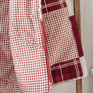 Close-up texture detail of red and white gingham check quilted cotton throw blanket hanging on wooden ladder