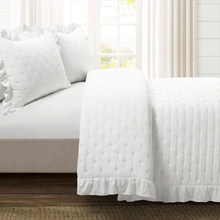 Close-up of white ruffle quilt bedding set with matching pillow shams