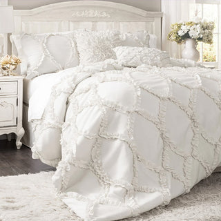 White cottage chic comforter with ruffle diamond pattern on bed with vintage white nightstand and floral arrangement