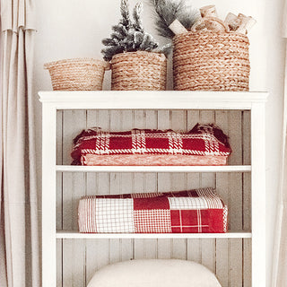 Christmas quilts folded and stacked on white shelves with wicker baskets for cozy farmhouse holiday storage display