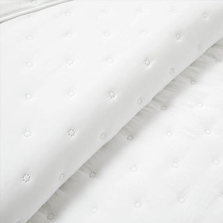 Folded white quilt showing textured embroidered details and soft ruffle edging