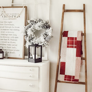 Red and white Christmas throw blanket displayed on rustic wooden blanket ladder next to white dresser with wreath