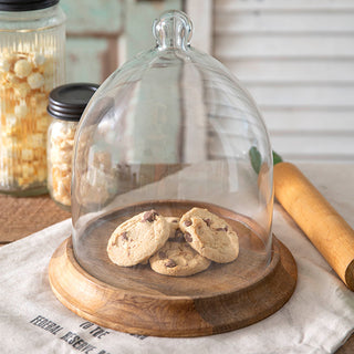 Glass cloche displaying chocolate chip cookies on wood base