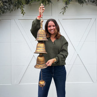 Woman holding a large hanging trio of distressed brass bells with star topper, displayed against a white barn-style backdrop