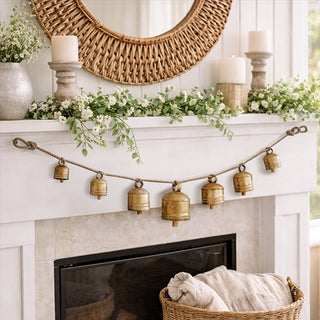 Brass metal bell garland draped on white fireplace mantel with greenery