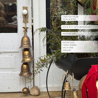 Distressed brass hanging bells with star topper displayed beside a rustic white door, surrounded by greenery and holiday decor elements