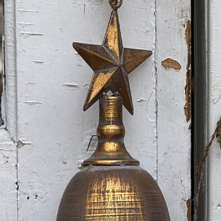 Close-up of distressed brass bell star topper showing rustic gold finish against a weathered white wooden background