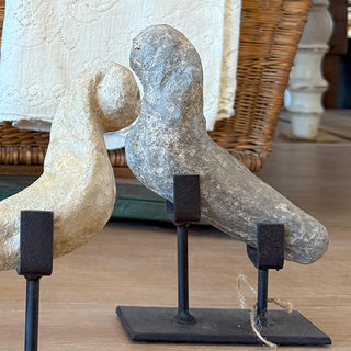 Two 17th century stone bird temple fragments in varying colors displayed on iron stands beside a wicker basket