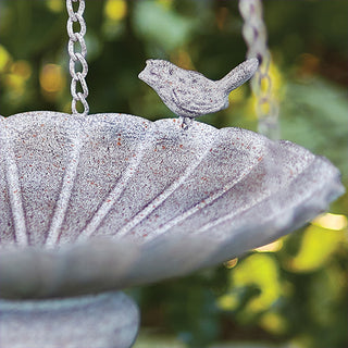Close-up detail of scalloped metal feeding pan showing distressed stone-gray finish and decorative bird figurine accent