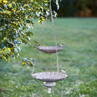  Vintage two-tier hanging bird feeder suspended from tree branch in lush green garden setting