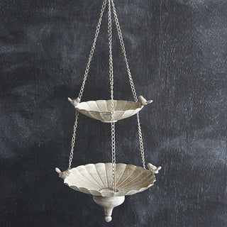 Full view of distressed metal two-tier hanging bird feeder showing scalloped edges and bird accents against dark background