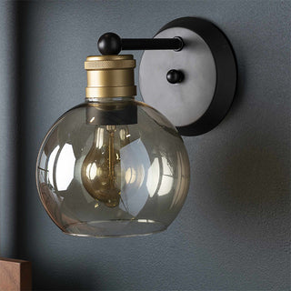 Wall-mounted light fixture with glass shade and metallic accents on a gray wall.