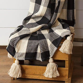 Close-up detail of black cream buffalo check blanket texture showing hand-woven cotton construction and decorative beige tassels on wooden ladder