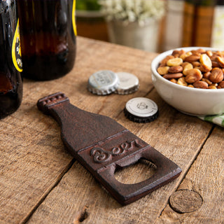 Vintage cast iron beer bottle opener on wooden table with beer bottle and snacks