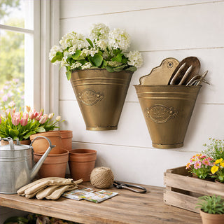Two distressed gold metal wall bucket planters hung on white shiplap wall in garden shed with white hydrangeas and garden tools