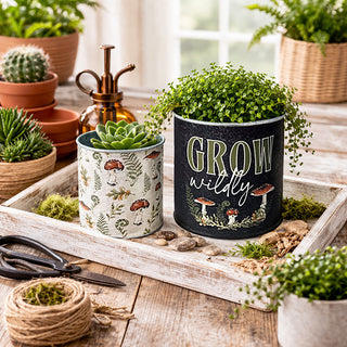 Two mushroom-themed metal buckets with plants on wooden garden tray with moss and gardening tools