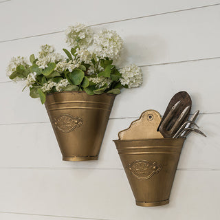 Two distressed gold metal wall buckets on white shiplap wall with white flowers and garden tools showing styling options