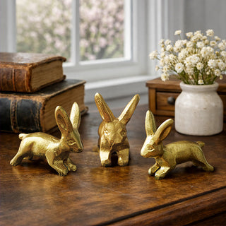Set of three distressed gold iron bunny figurines on wooden tabletop with vintage books