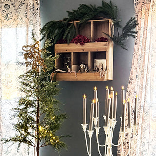 Rustic wooden cubby wall shelf decorated with greenery, florals, and vintage accessories in a cozy holiday room setting.