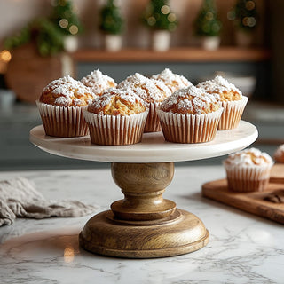 Rustic marble and wood cake stand displaying fresh muffins dusted with powdered sugar on a modern kitchen countertop.