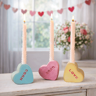 Three clay conversation heart candle holders in pastel blue pink and yellow with HUGS XOXO LOVE messages holding taper candles Valentine's Day tablescape decor