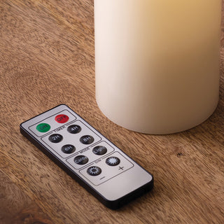 Remote control for LED candles showing timer and brightness adjustment buttons next to ivory candle