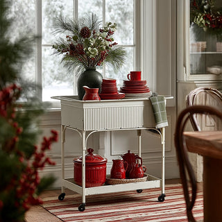 Distressed white metal bar cart with corrugated panel styled with red dishes and holiday decor by window