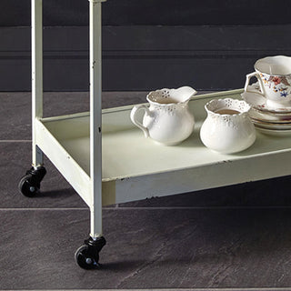 Bottom shelf detail of white metal bar cart showing four rolling wheels and painted finish